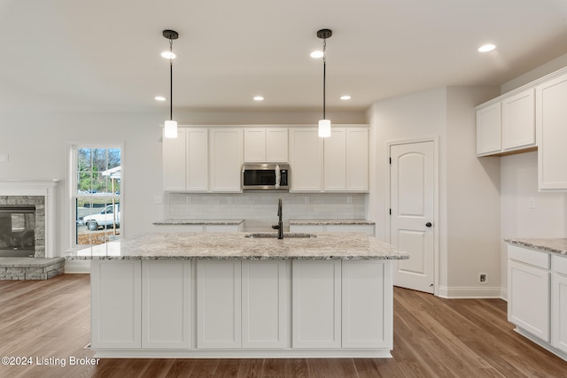 kitchen with pendant lighting, light wood-type flooring, white cabinets, and an island with sink