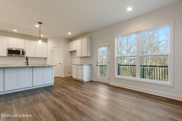 kitchen with white cabinetry, light stone counters, hanging light fixtures, dark wood-type flooring, and decorative backsplash