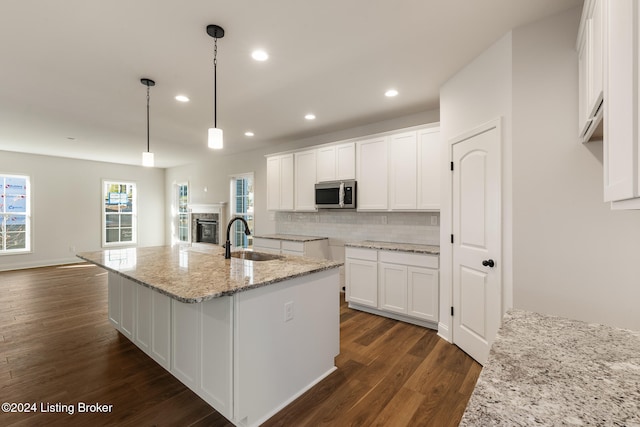 kitchen with light stone counters, white cabinetry, dark hardwood / wood-style floors, sink, and an island with sink