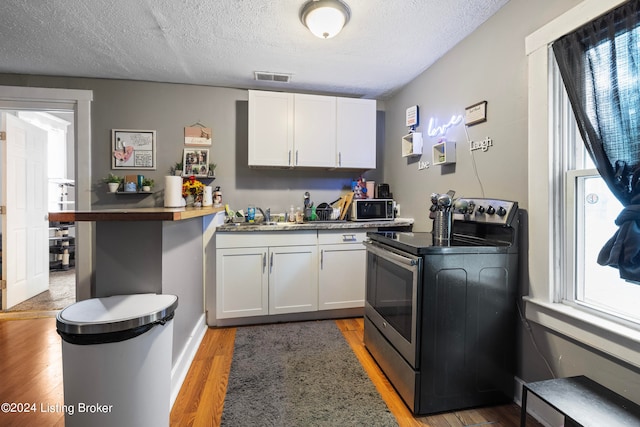 kitchen featuring white cabinetry, stainless steel electric stove, a textured ceiling, and hardwood / wood-style flooring