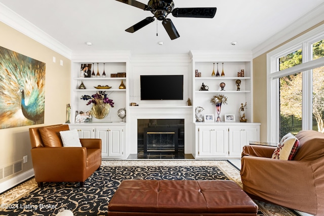 living room featuring crown molding, a tiled fireplace, built in features, and ceiling fan