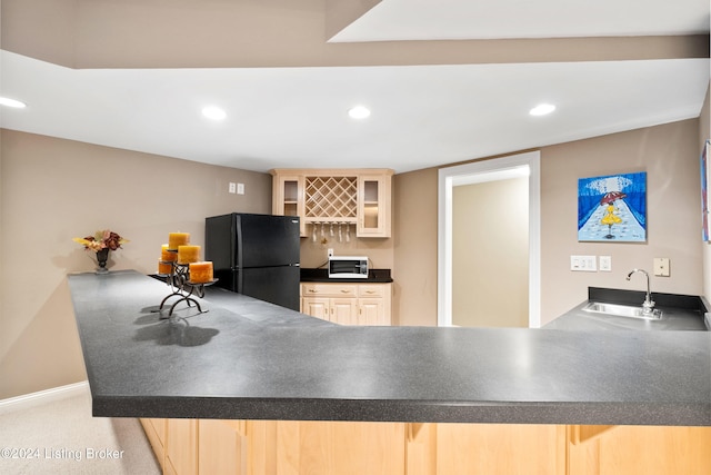 kitchen with light carpet, light brown cabinets, kitchen peninsula, black refrigerator, and sink