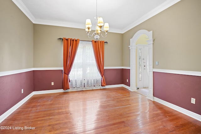 unfurnished room featuring ornate columns, hardwood / wood-style flooring, crown molding, and an inviting chandelier