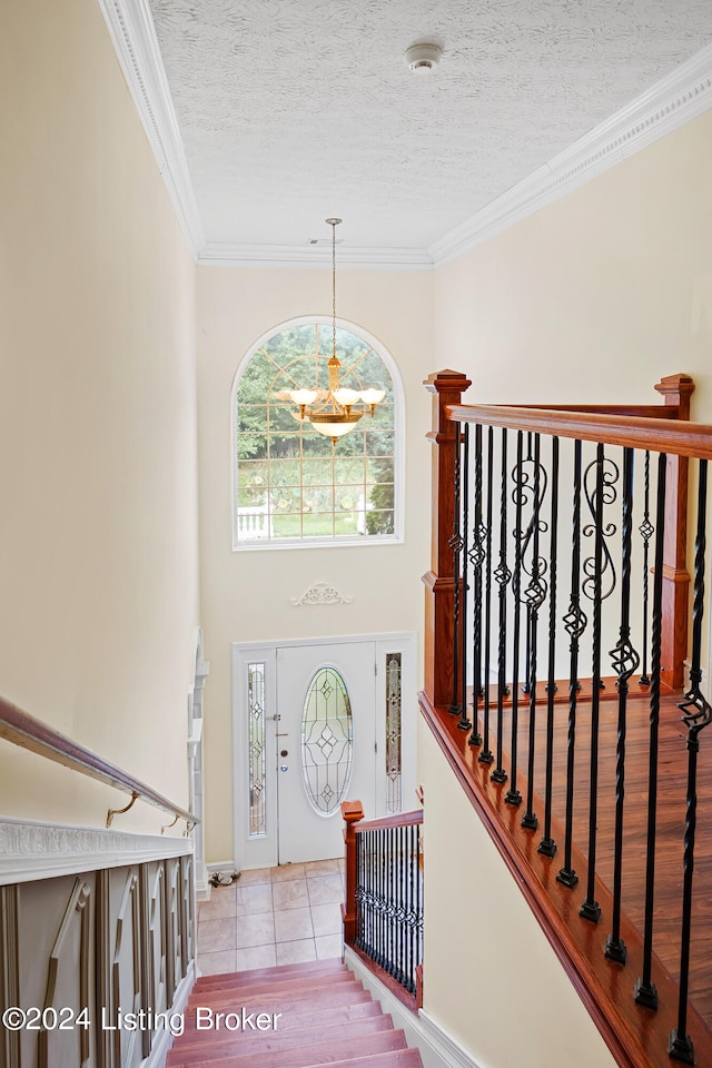 entrance foyer with light wood-type flooring, a notable chandelier, crown molding, and a textured ceiling