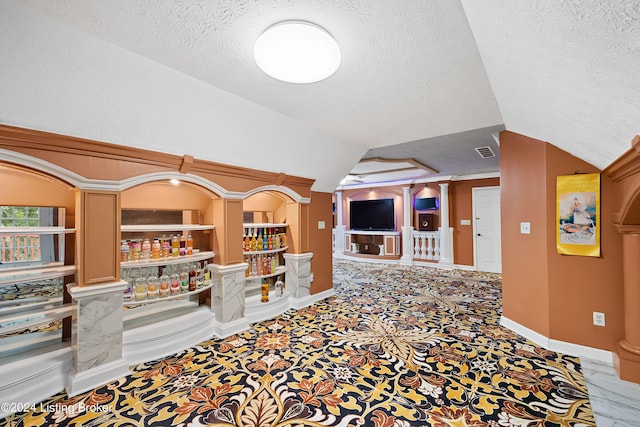 interior space featuring built in shelves, vaulted ceiling, and a textured ceiling