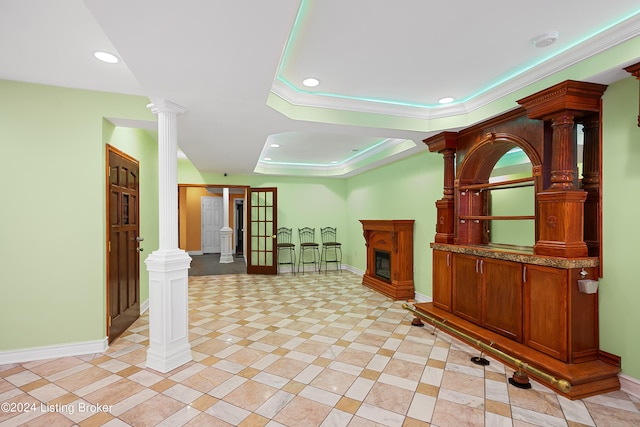 interior space with a raised ceiling, crown molding, and decorative columns