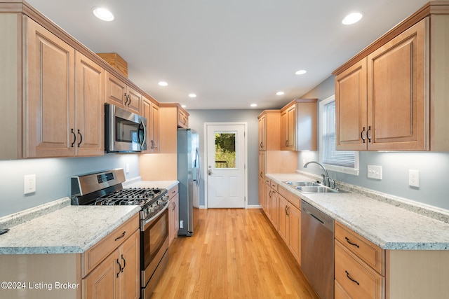 kitchen featuring stainless steel appliances, light stone countertops, sink, and light wood-type flooring