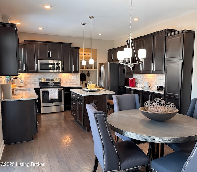 kitchen featuring appliances with stainless steel finishes, a kitchen island, decorative light fixtures, dark wood-type flooring, and decorative backsplash