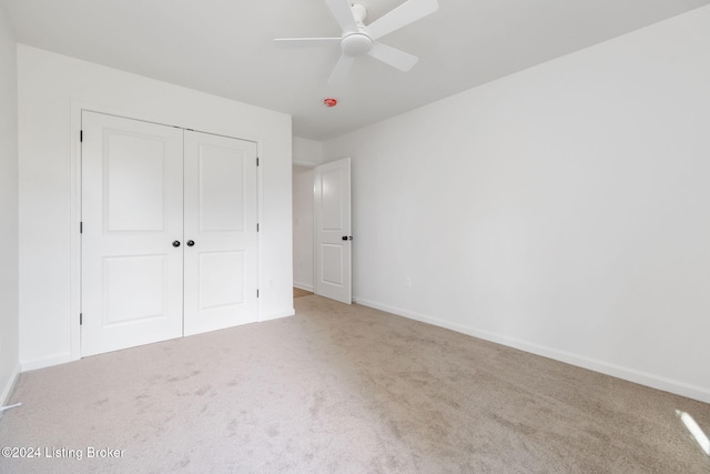 unfurnished bedroom featuring a closet, light colored carpet, and ceiling fan