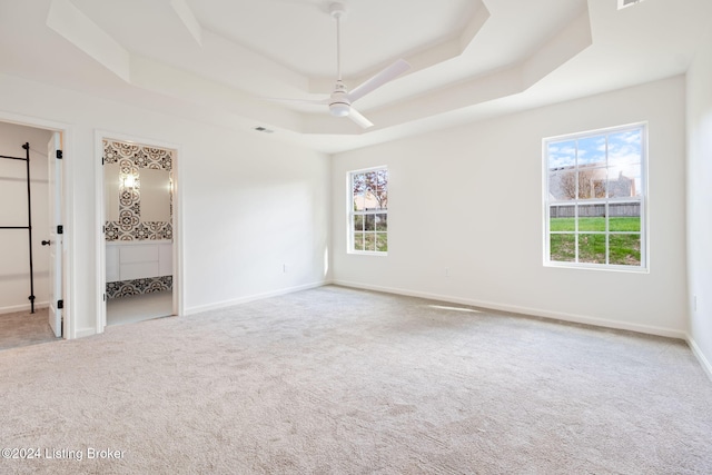 unfurnished bedroom featuring a tray ceiling, multiple windows, and ceiling fan