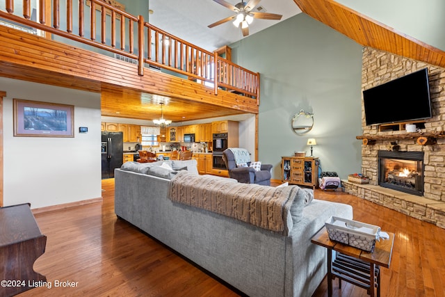 living room with ceiling fan with notable chandelier, light hardwood / wood-style floors, high vaulted ceiling, and a stone fireplace