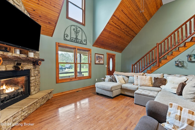 living room with a stone fireplace, light hardwood / wood-style floors, high vaulted ceiling, and wooden ceiling