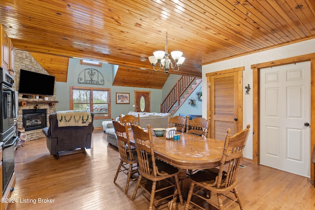 dining area with wooden ceiling, a notable chandelier, light wood-type flooring, and a stone fireplace