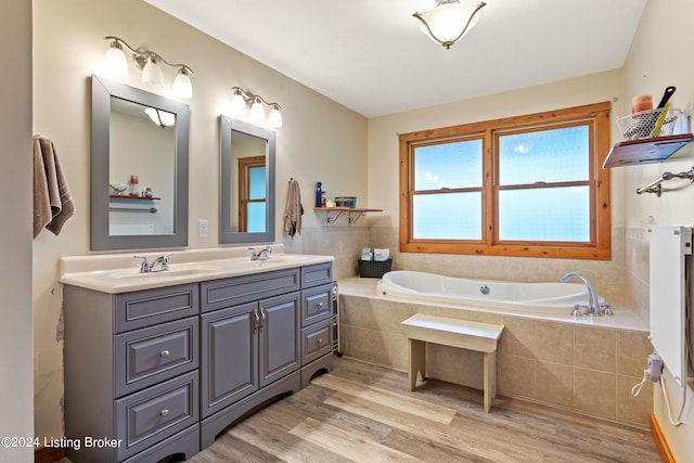 bathroom featuring hardwood / wood-style floors, a relaxing tiled tub, and vanity