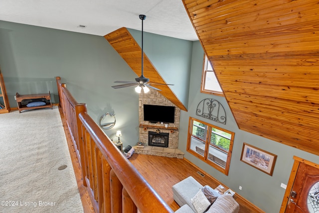 living room with carpet floors, ceiling fan, high vaulted ceiling, and a stone fireplace