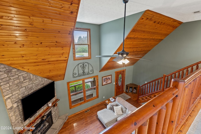 living room with ceiling fan, a stone fireplace, hardwood / wood-style flooring, vaulted ceiling, and a textured ceiling