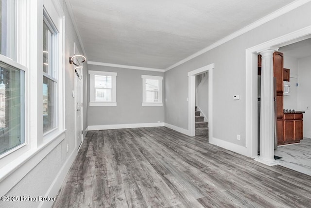 spare room featuring decorative columns, ornamental molding, light wood-style floors, baseboards, and stairs