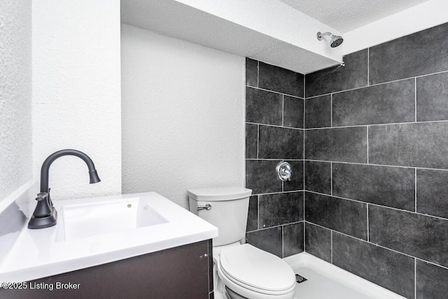 bathroom featuring a textured wall, toilet, vanity, a textured ceiling, and tiled shower