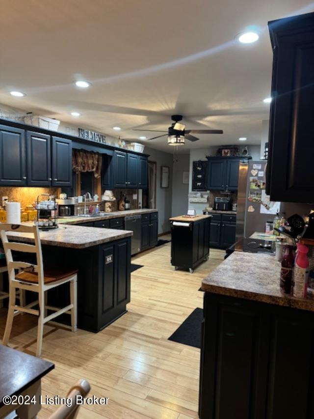 kitchen with a peninsula, a ceiling fan, freestanding refrigerator, a center island, and light wood finished floors