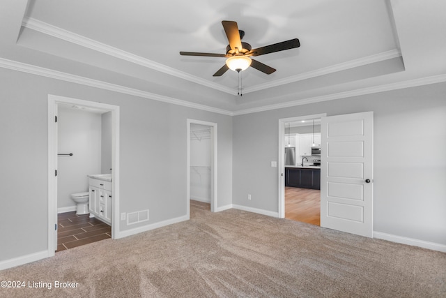 unfurnished bedroom featuring dark colored carpet, ensuite bathroom, ceiling fan, and a raised ceiling