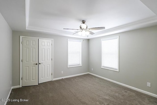 unfurnished bedroom with ceiling fan, multiple windows, dark carpet, and a tray ceiling