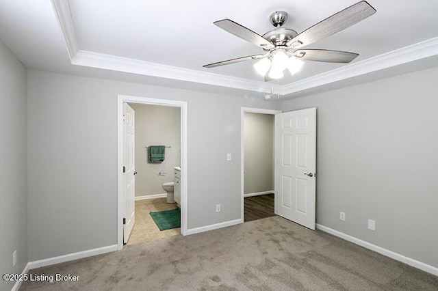 unfurnished bedroom featuring connected bathroom, ceiling fan, a tray ceiling, and light colored carpet