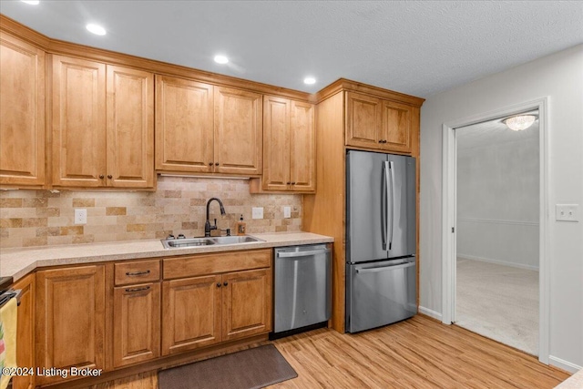 kitchen with decorative backsplash, a textured ceiling, light wood-type flooring, sink, and stainless steel appliances