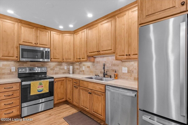 kitchen with sink, decorative backsplash, stainless steel appliances, and light wood-type flooring