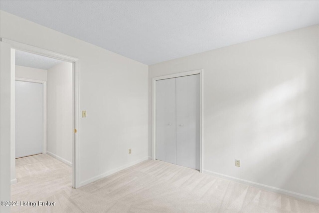 unfurnished bedroom with light carpet, a textured ceiling, and a closet