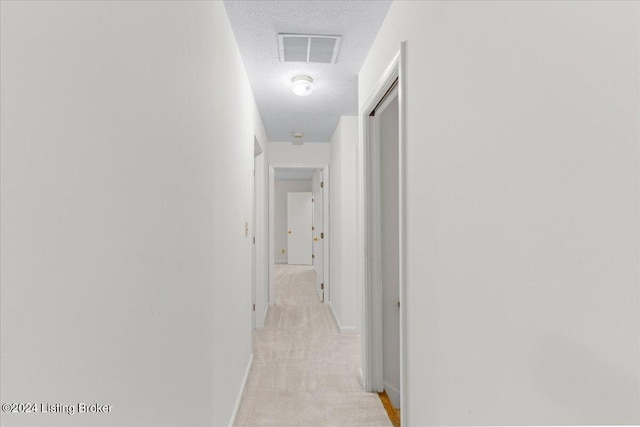 hall with light carpet and a textured ceiling