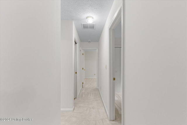 hall with a textured ceiling and light colored carpet