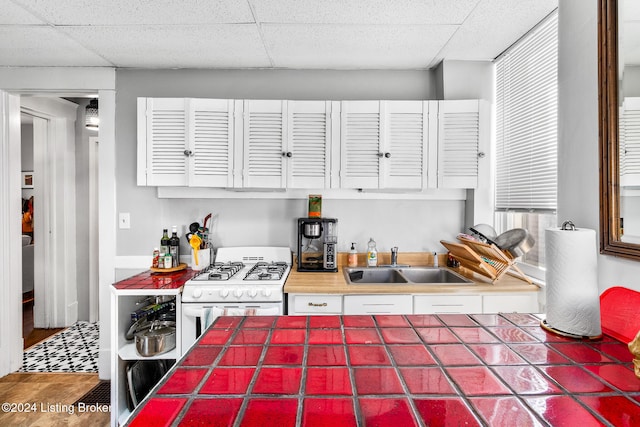 kitchen with tile countertops, gas range gas stove, a paneled ceiling, and sink