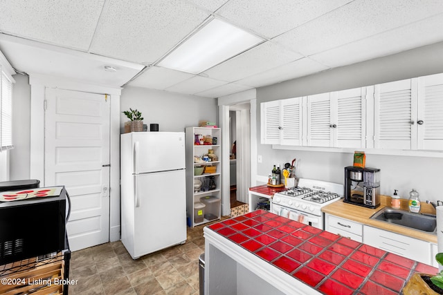 kitchen featuring white appliances, sink, tile countertops, a paneled ceiling, and white cabinets