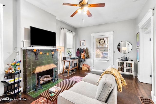 living room featuring dark wood-type flooring, ceiling fan, and a tiled fireplace