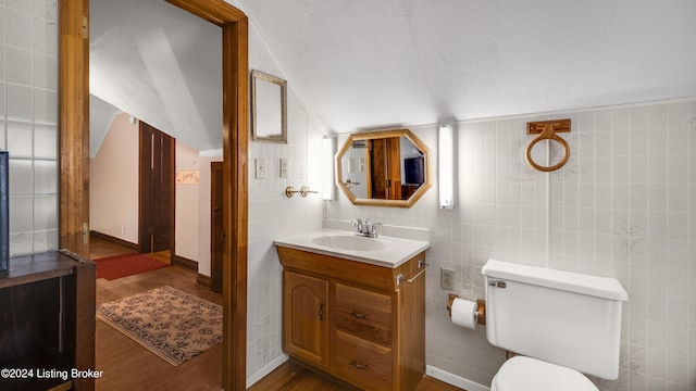 bathroom featuring hardwood / wood-style floors, tile walls, vaulted ceiling, toilet, and vanity