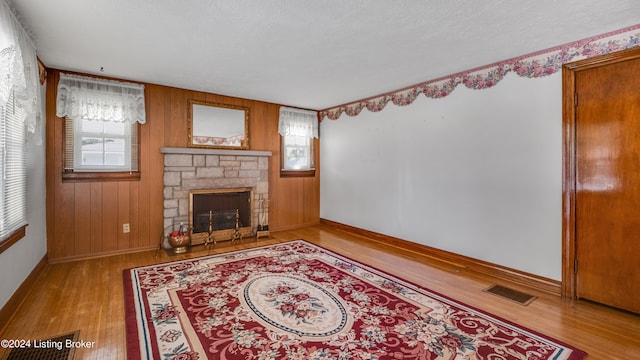 living room featuring a textured ceiling, a fireplace, light hardwood / wood-style floors, and wood walls