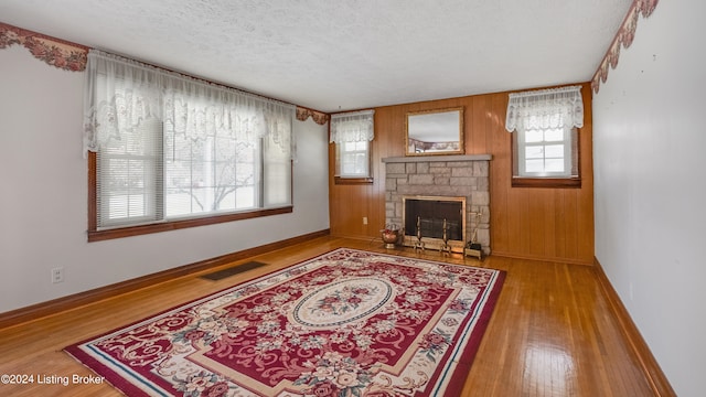 living room featuring hardwood / wood-style floors, a stone fireplace, a textured ceiling, and wood walls