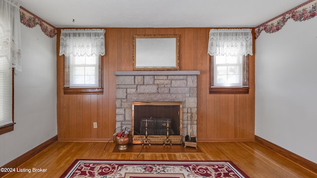 unfurnished living room featuring light hardwood / wood-style floors, a healthy amount of sunlight, wooden walls, and a fireplace