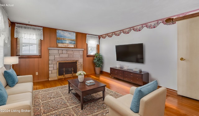 living room with a stone fireplace, wood-type flooring, and wood walls