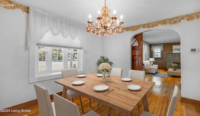 dining room with a stone fireplace, an inviting chandelier, and hardwood / wood-style floors