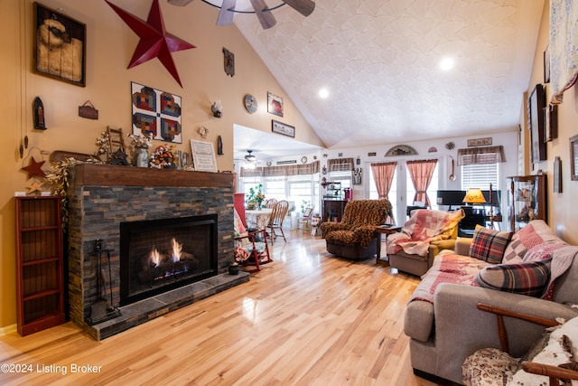 living room featuring a stone fireplace, high vaulted ceiling, wood-type flooring, and ceiling fan