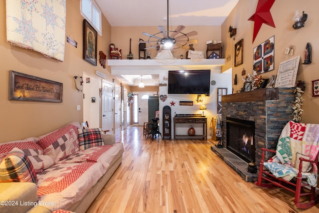 living room with ceiling fan, a stone fireplace, and light wood-type flooring