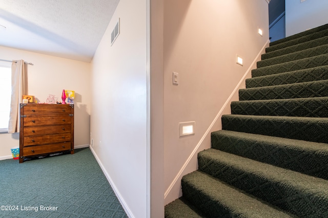 stairs with a textured ceiling and carpet flooring