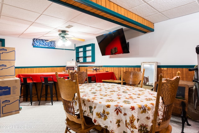 carpeted dining space with wooden walls, a paneled ceiling, and ceiling fan