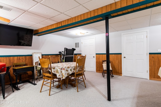 dining space featuring wooden walls, a paneled ceiling, and light colored carpet