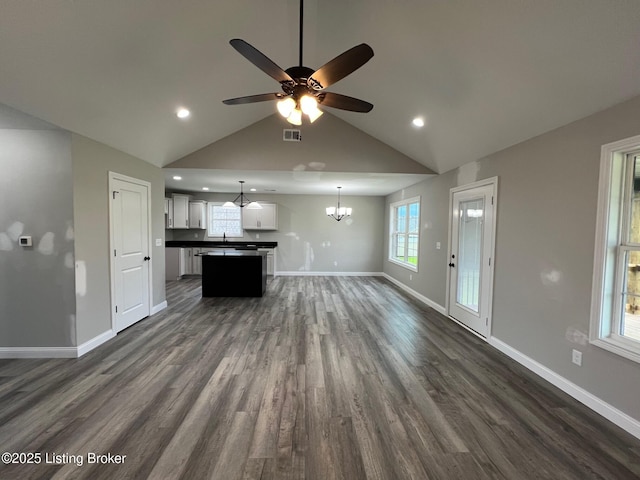 unfurnished living room with dark wood-type flooring, visible vents, vaulted ceiling, baseboards, and ceiling fan with notable chandelier