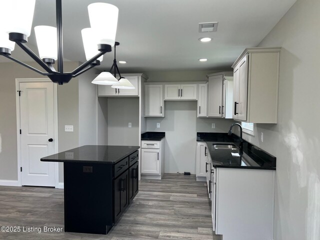 kitchen featuring a kitchen island, dark countertops, light wood finished floors, and a sink