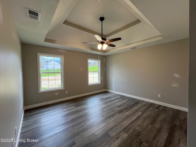 spare room with dark wood-style flooring, a raised ceiling, a ceiling fan, and visible vents
