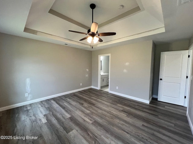 unfurnished bedroom featuring ensuite bathroom, baseboards, visible vents, a raised ceiling, and dark wood-type flooring