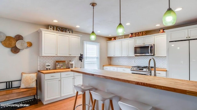 kitchen with appliances with stainless steel finishes, white cabinetry, light wood-type flooring, wooden counters, and decorative light fixtures